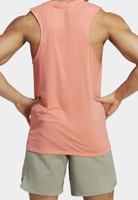 Canottiera leggera senza maniche in morbido tessuto corallo. Presenta una vestibilità comoda e un collo arrotondato, abbinata a pantaloni corti grigi chiari.