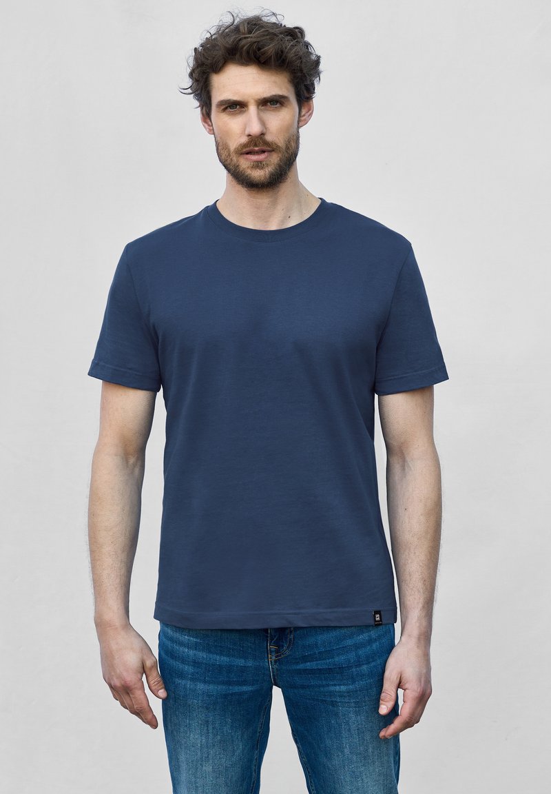 Námořnická modrá bavlněná tričko s krátkými rukávy, kulatým výstřihem a uvolněným střihem. Obsahuje malou logo dekoraci blízko lemu, kombinované s modrými džíny.