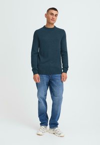 Donker tealen gebreide trui met een ronde halslijn, gecombineerd met lichtblauwe spijkerbroeken en witte sneakers. Eenvoudige textuur met aansluitende manchetten.