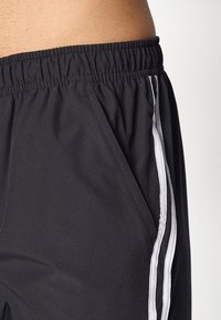 Pantalones cortos deportivos negros con una cinturilla elástica, que presentan dos franjas verticales blancas a lo largo de los lados y una tela texturizada.