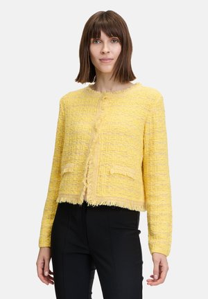 Gelbe strukturierte Tweedjacke mit fransigem Saum, rundem Halsausschnitt, Knopfverschluss und zwei vorderen Taschen. Kurze Ärmel und verkürzter Schnitt.