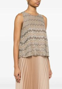 Top beige senza maniche con una vestibilità ampia, caratterizzato da un delicato motivo a zigzag in fili metallici. Abbinato a una gonna plissettata di un leggero beige.