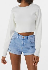 White ribbed crop top with long sleeves, paired with light blue high-waisted denim shorts featuring a rolled hem and distressed details.