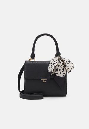 Sac à main en cuir noir texturé avec poignée supérieure, bandoulière amovible, fermeture à clip en or et foulard blanc à pois noirs attaché à la poignée.