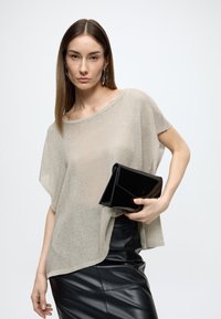 Top tricotat bej deschis cu croială lejeră, asortat cu o geantă clutch neagră lucioasă. Ținuta include o fustă neagră din piele, mulată.