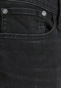 Gros plan de la poche d'un jean en denim noir avec des rivets métalliques gravés du nom de la marque "Jack & Jones".