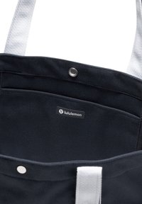 Crna platnena torba sa srebrnim dodacima, izdržljivim trakama, unutarnjim džepom i ruhom s lululemon oznakom.