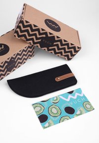 Black felt eyeglass case with a curved shape and brown leather accent. Two brown cardboard boxes with black zigzag patterns. Colorful kiwi-patterned card.