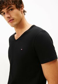 Camiseta negra de cuello en V hecha de un tejido suave, con mangas cortas y un pequeño logotipo bordado en rojo, blanco y azul en el pecho.