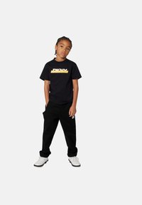 Zwarte t-shirt met een gele DKNY-logo, gecombineerd met zwarte cargo-broek met zakken, en witte sneakers met grijze zolen.