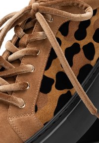 Sneaker in suede marrone con un pannello tessile a stampa leopardo, lacci tondi beige e occhielli dorati. Suola in gomma nera e superficie texture.