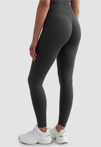Ciemnoszare legginsy z wysokim pasem, gładką fakturą i dopasowanym krojem. Połączone z białymi sportowymi butami dla kontrastu.