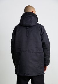 Zwarte gewatteerde jas met een hoge kraag, voorzien van een ritssluiting en een zachte, getextureerde voering. Het ontwerp heeft een detail aan de achterkant en een ontspannen pasvorm.