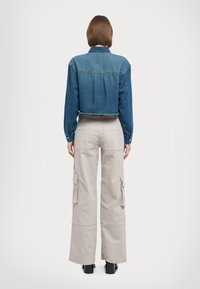 Giacca di jeans cropped blu scuro con maniche lunghe, polsini con bottoni e orlo grezzo. Abbinata a pantaloni cargo beige chiaro con gamba larga e tasche laterali.