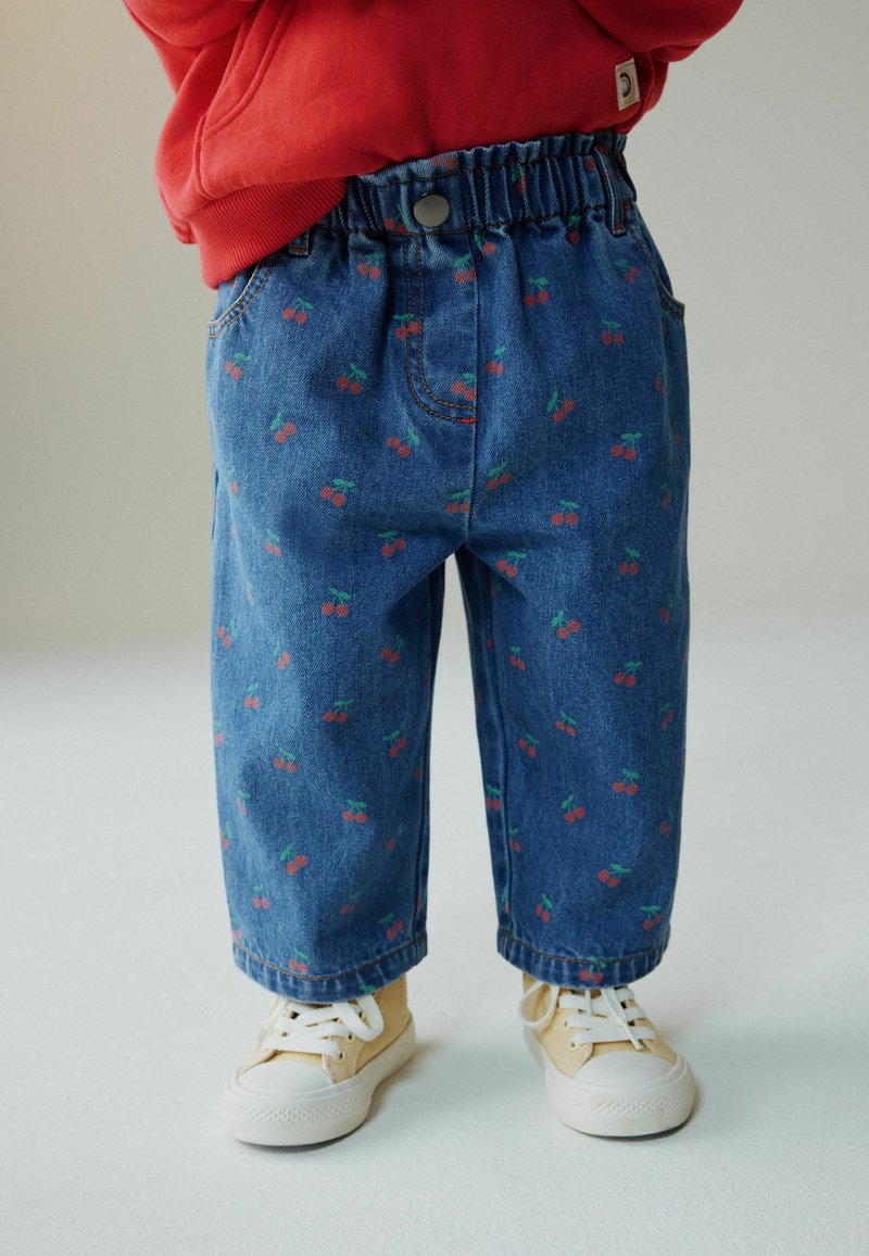 Pantalones de mezclilla azul con cintura elástica y estampado de cerezas. Combinados con zapatillas beige y sudadera roja.