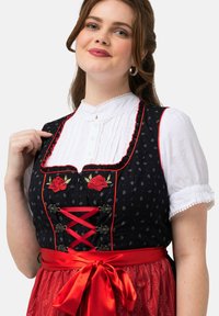Traditioneel kostuum met een zwarte lijfje met rode bloemenborduring, een witte bloes en een vloeiende rode rok met een satijnen riem.