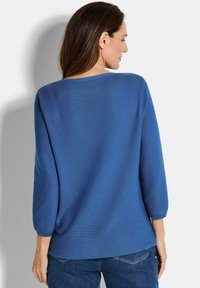 Blauwe, geribbelde gebreide trui met driekwartmouwen, ronde halslijn en een losse pasvorm; gecombineerd met denim jeans.