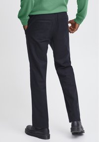 Pantaloni blu navy in cotone con una texture liscia, dotati di due tasche posteriori e un design a gamba dritta, abbinati a stivaletti neri alla caviglia.