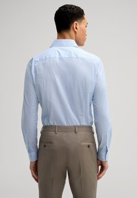 Chemise à manches longues bleu clair avec un petit motif à pois, associée à un pantalon habillé marron clair, comportant des poches arrière et un détail de bouton.