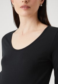 Crni dolgi rukav majica od rasteznog materijala, sa širokim izrezom i glatkom teksturom, u uskom kroju.