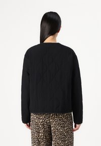 Black quilted jacket with a rounded neckline and long sleeves. Features a textured wave pattern, worn over animal print pants.