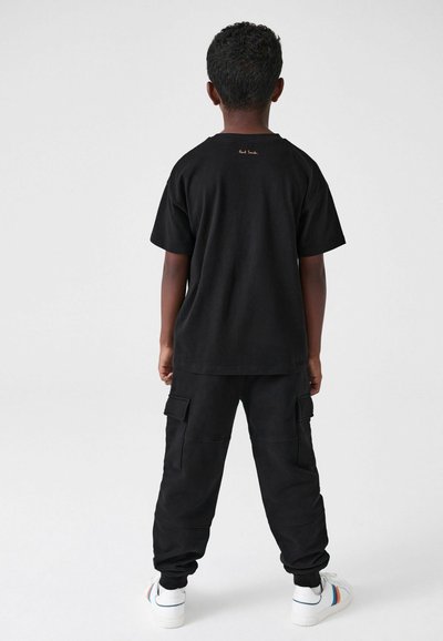 Mustat puuvillateepaidat, joissa on lyhyet hihat ja takapuolella oranssia logotyttöä. Yhdistetty mustiin cargo-housuihin, joissa on sivutaskut ja elastiset resorit.