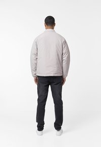 Svetlosivá vypchatá bunda s cropped strihom, elastickými manžetami a chrbátom, skombinovaná s tmavými džínami a bielymi teniskami.