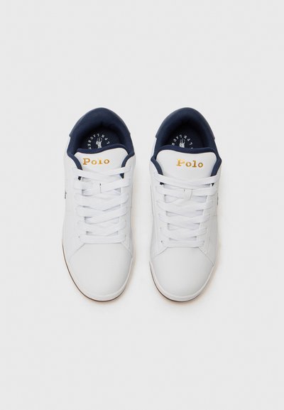Baskets blanches avec une finition en cuir lisse, dotées de lacets blancs, d'accents marins sur le col et d'un logo doré "Polo" sur la languette.