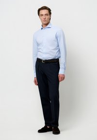 Lichtblauw overhemd met knopen, marineblauwe broek, zwarte riem, bruine schoenen. Het overhemd heeft lange mouwen, een slim fit, een klassieke kraag en een subtiele textuur.