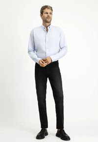 Camicia leggera azzurra con colletto, abbinata a jeans di denim neri e scarpe stringate nere. Design semplice e su misura.