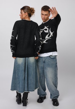 Black knit sweater with white flame pattern on sleeves, paired with a long light blue denim skirt and baggy blue jeans, black boots.