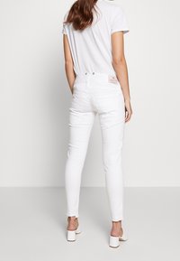 Białe jeansy skinny z wysokim stanem i lekko postrzępionym dołem. Z tyłu znajdują się kieszenie naszyte oraz metka marki umieszczona nad pasem.