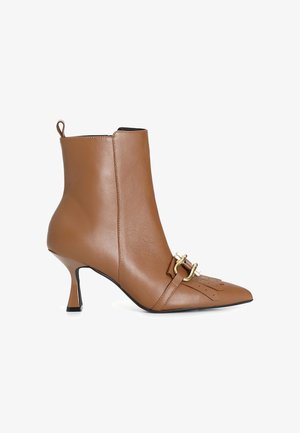 Bottine en cuir marron à bout pointu, avec un détail de boucle en or et un talon incliné. Texture lisse avec des accents de couture minimalistes.
