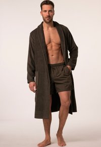 Brauner Frottee-Bademantel mit langen Ärmeln und vorderen Taschen, getragen über olivgrünen Schwimmshorts, der eine entspannte Passform und weiche Textur zeigt.