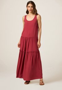 Abito lungo senza maniche di colore rosso realizzato in un tessuto morbido, con vita arricciata e gonna a strati. Design semplice con una silhouette fluida.