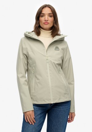 Lichtgroene waterdichte jas met een capuchon, rits aan de voorkant, twee zijzakken en een logo op de borst. Glad textuur, aansluitend design.