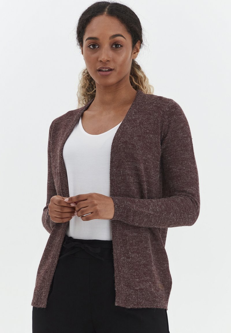 Cardigan en tricot bordeaux avec manches longues, design à l'avant ouvert et poignets côtelés. Porté sur une chemise blanche, en tissu doux et texturé.