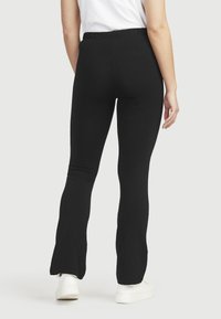 Zwarte flared leggings van rekbaar materiaal met een elastische tailleband. De stof lijkt glad met een aansluitende silhoeet.