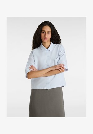 Camisa de manga corta azul clara con cuello, cierre de botones en el frente y un solo bolsillo en el pecho. Tejido suave, diseño corto.