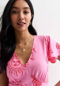 Rosa klänning med röda abstrakta mönster, V-ringning och svävande ärmar. Kommer med en guldkedja med hänge. Mjuk tygtextur.