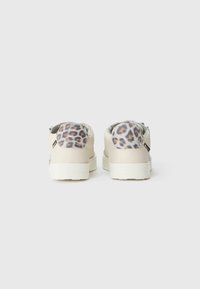 Cream-colored sneakers featuring a plush leopard print panel at the heel, rubber sole, and minimalistic design with grey accents.