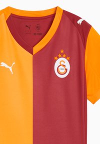 Maglietta a maniche corte rossa e arancione con scollatura a V, caratterizzata da un logo centrale e cinque stelle sopra. Realizzata in un morbido poliestere con il marchio Puma.