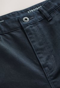 Mørkeblå denimbukser med lige pasform, knaplukning og synlige syningsdetaljer. Mærkevarenavn vist inde i linningen.