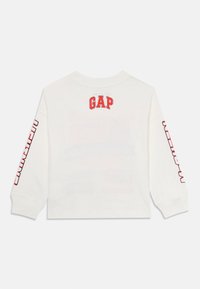 Hvit langermet skjorte med rødt "GAP"-logo på baksiden og rødt tekst langs ermene. Laget av mykt bomullsmateriale.
