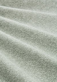 Textielstof in lichtgroen met een getextureerd patroon, met zachte, geplooide lagen. De weving is strak en uniform, wat de visuele diepte versterkt.