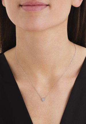 Krupan plan osobe koja nosi nježnu srebrnu ogrlicu s malim privjeskom u obliku srca ukrašenim sitnim kristalima.