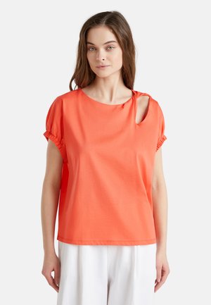 Camisa corta de manga en tejido suave, de color coral, con escote redondo, detalle en forma de ojal en el hombro y mangas fruncidas con acentos elásticos.