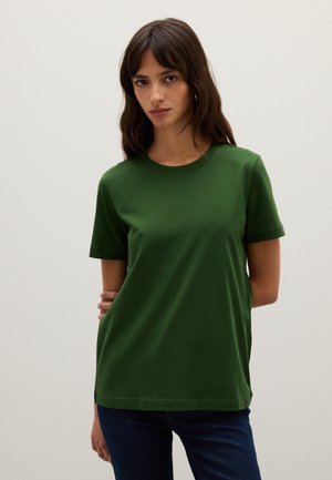 Groene kortekraag t-shirt van zacht materiaal met een ronde hals, heeft een rechte snit en minimale details. Draagt een blauwe spijkerbroek.