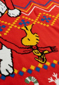 Tessuto lavorato a maglia rosso con un uccellino giallo in stile cartoon, zampe bianche e motivi geometrici colorati in blu e giallo. Elementi di design testurizzati e giocosi.