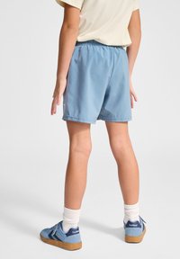 Blå lätta shorts med elastisk midja, slät yta och sidofickor. Bärs med vita strumpor och blå sneakers.